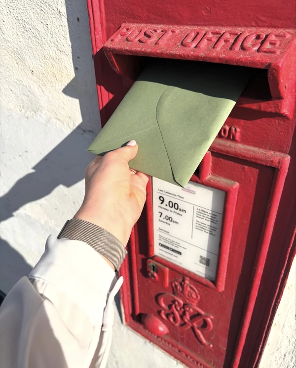 A hand posting a green Taletrove envelope into a red post box